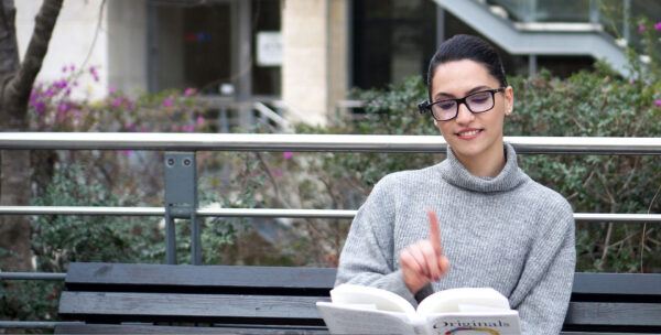 OrCam junge Frau auf Parkbank liest Buch